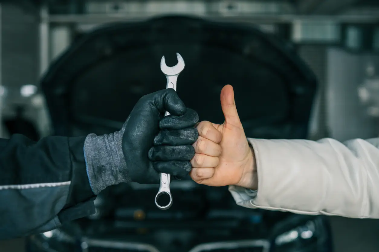Mechanic holding wrench, customer giving thumbs up.