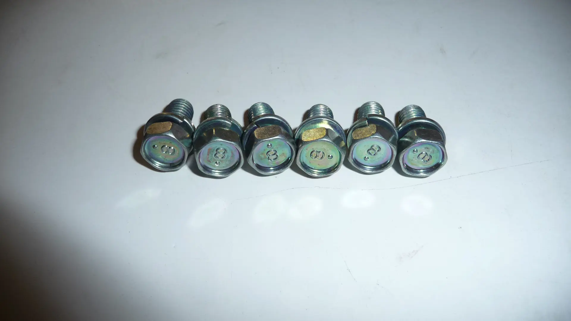 Six metal bolts on a white surface.