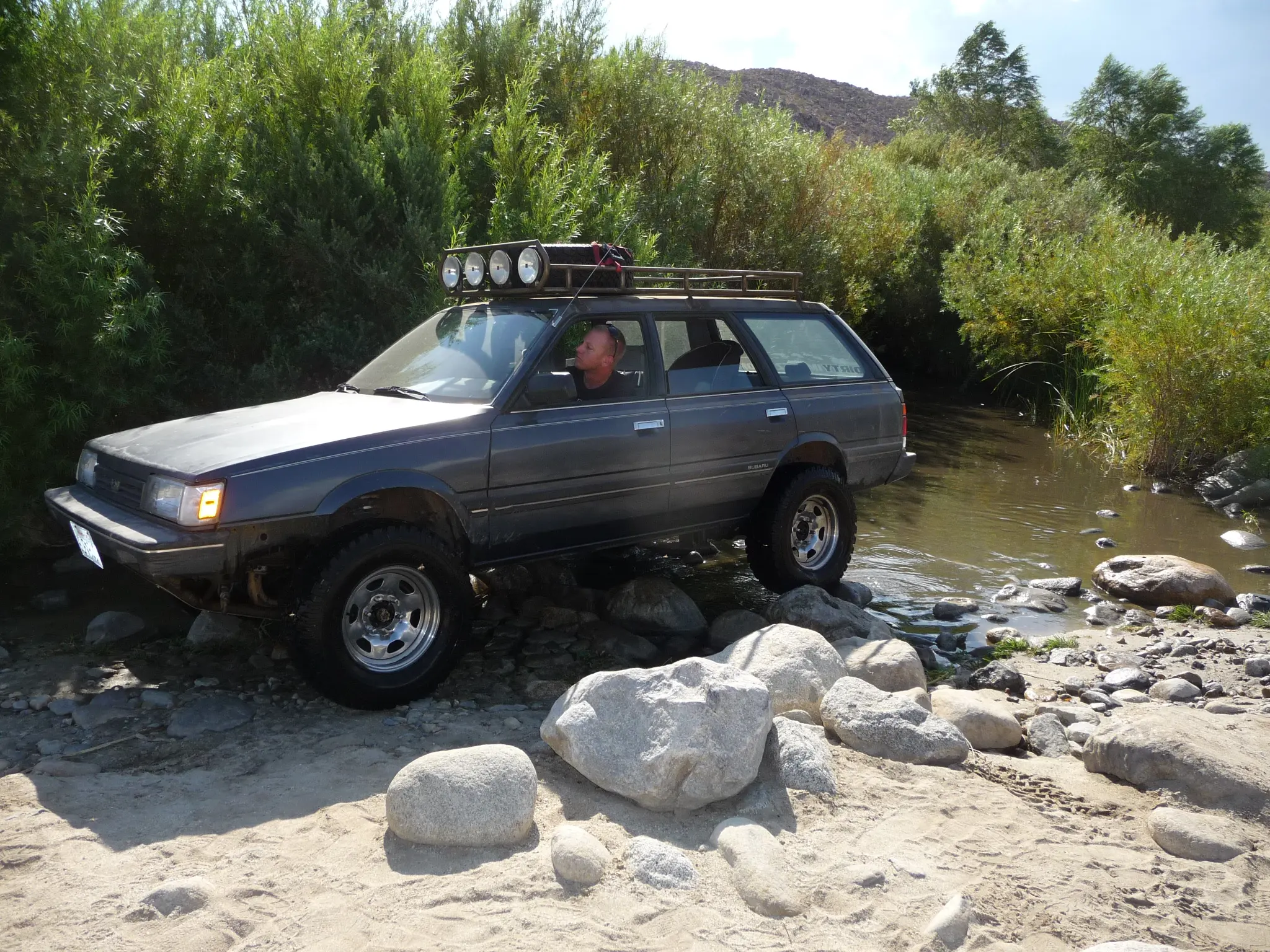 Off-road SUV crossing a shallow rocky stream in a natural setting.