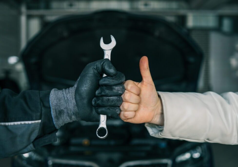 Mechanic holding wrench, customer giving thumbs up.